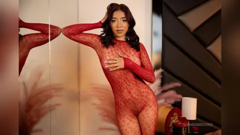 Young woman in a red lace bodysuit posing elegantly in a warm, modern interior setting.