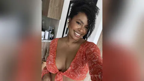 Smiling Black woman in a red patterned wrap top posing in a bright modern kitchen.