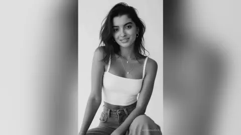 Smiling young woman in a white tank top and denim jeans posing for a minimalist black and white portrait.
