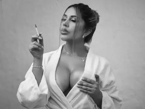 Glamorous woman in a white robe smoking a cigarette against a plain background in a moody black and white portrait.