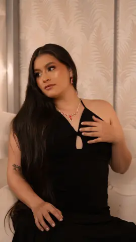 Elegant woman in a black halter dress and red necklace posing gracefully in a bright, modern room.