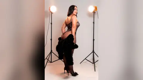 Glamorous woman in black lace bodysuit and faux fur wrap posing in a professional photo studio.