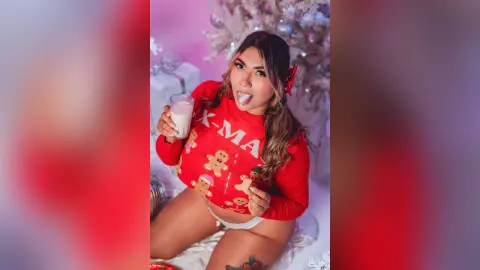Smiling woman in a red Christmas sweater holding milk near a festive holiday tree.