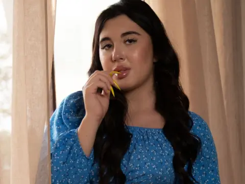 Young woman in a blue floral blouse posing thoughtfully by a window with soft natural lighting.