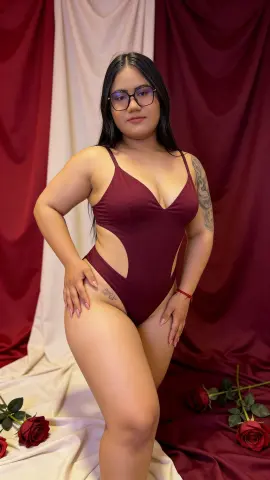 Lizzyolsen90 wears a maroon bodysuit while posing against a red and white draped fabric background.