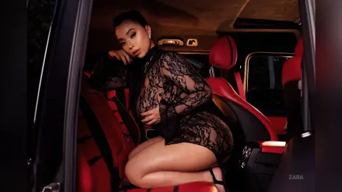 Glamorous woman in a black lace sheer dress sitting in a luxury red leather car interior.