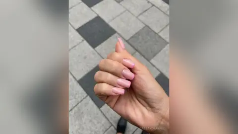 Close-up of a hand with elegant light pink manicured nails against a grey checkered stone pavement background.