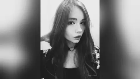 Moody black and white portrait of a young woman with long hair wearing a heart choker necklace.