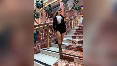 Stylish woman in a black blazer and mini skirt posing on marble stairs in a luxury hotel lobby.