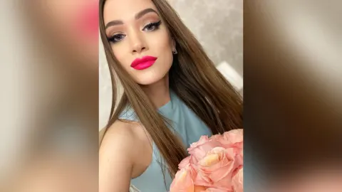 AlienaMoore — AlienaMoore with long brown hair and bright pink lipstick poses with pink roses.