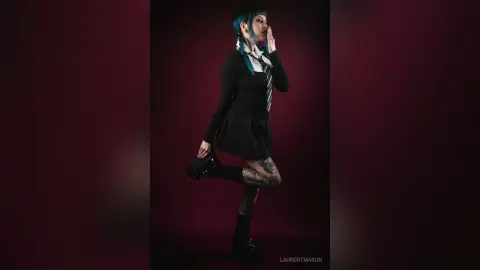 Moody portrait of a blue-haired woman in a black schoolgirl outfit posing against a dark background.