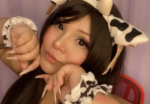 Young woman in cow print headband and accessories posing with a playful expression against a purple background.