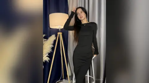 Elegant woman in a sleek black long-sleeve midi dress posing in a moody, minimalist indoor studio setting.