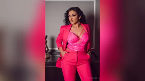 Elegant woman in a hot pink power suit and lace corset posing confidently in a studio setting.