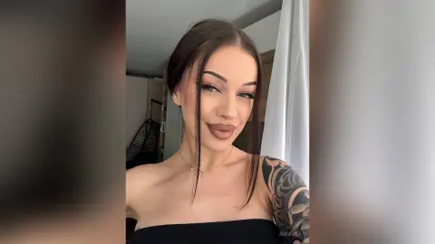 AriaVex poses with long dark hair and heavy eyeliner, wearing a black tube top and showing a large black tattoo on her shoulder.
