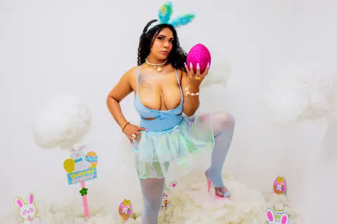 Curvy woman in a blue bunny costume holding a pink glitter egg in a dreamy white cloud Easter setting.