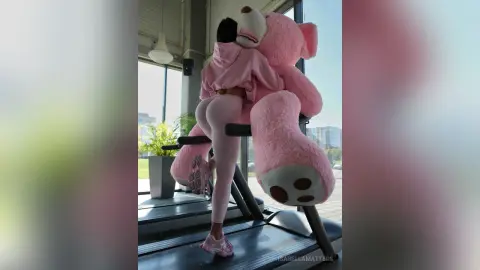 Woman in pink loungewear hugging a giant pink teddy bear in a bright modern room.