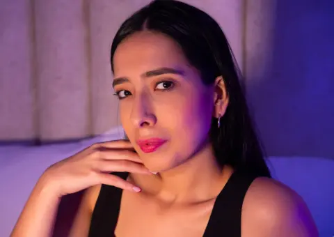 Young woman in a black tank top posing with a thoughtful expression under moody purple lighting.