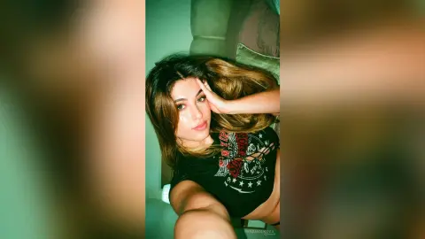 IrinaMolkova poses wearing a black graphic t-shirt, running her hand through her long brown hair.