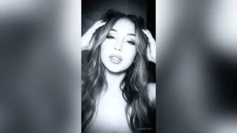 MeganLewit poses with her hands in her long wavy hair, looking into the camera in this black and white shot.