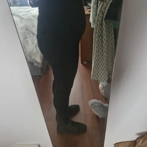 Person in casual black loungewear and fuzzy slippers standing in a cozy bedroom mirror reflection.
