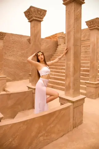 Woman in white bohemian crop top and skirt posing in ancient stone ruins under a warm desert sun.