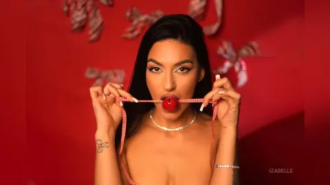 Iza — Young woman with long dark hair holding red checkered ribbon against a red background in a playful mood.
