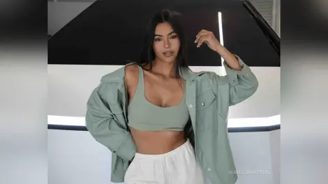 Young woman in a sage green crop top and open button-down shirt posing in a modern minimalist studio.