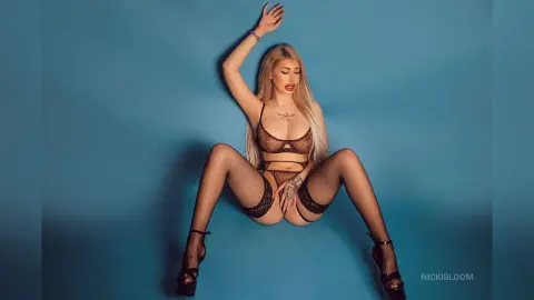ViviAnne — NickiBloom poses in black lace lingerie and fishnet stockings against a blue background.