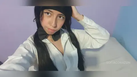 SofiaCorazon wearing a white button-down shirt and a black bow, posing with her hand in her long black hair against a purple wall.