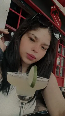 Young woman with dark hair enjoying a refreshing lime margarita at an outdoor cafe.