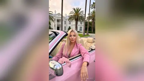 Blonde woman in a pink blazer sitting in a vintage pink convertible parked near a luxury white mansion.