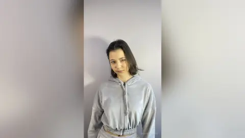 Young woman in a cozy grey hoodie posing against a minimalist neutral wall in a relaxed mood.