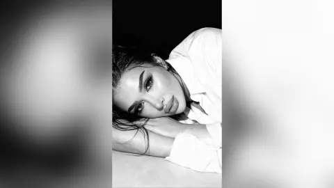 Moody black and white portrait of a young woman in a white shirt resting her head on her arms.