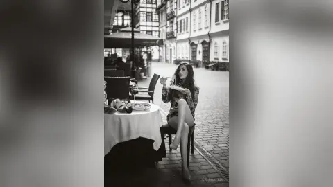 Elegant woman in a patterned blouse dining at an outdoor cafe on a European cobblestone street.