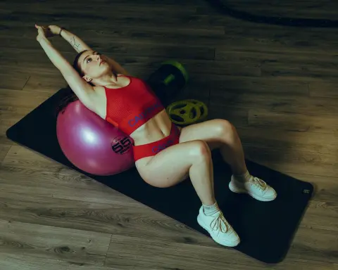 DaniRosexx wearing a red Calvin Klein sports bra and red undies, sitting on a pink exercise ball on a black mat.