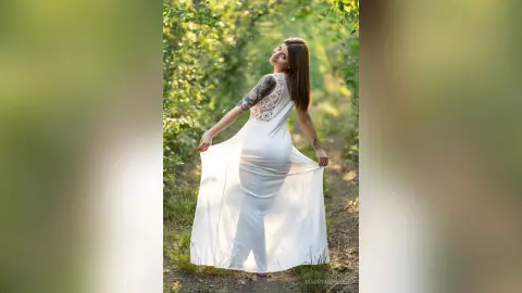 MarryMenedez poses in a white dress outdoors, looking back over her shoulder with her long hair down.