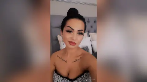 Glamorous woman with a high bun and sparkly top posing in a cozy bedroom setting.