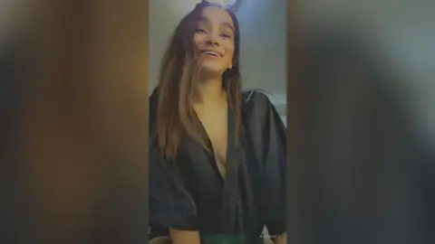Smiling young woman in a black satin robe relaxing in a dimly lit room.
