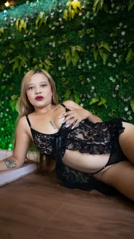 Woman in black lace lingerie relaxing against a lush green leaf wall background.