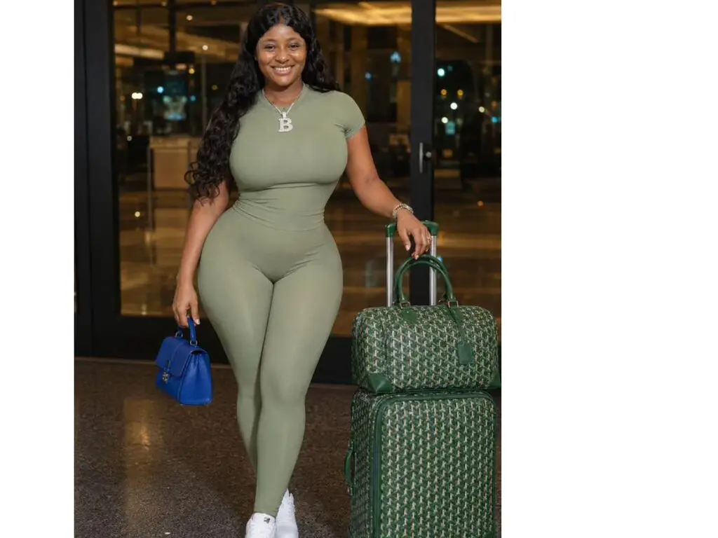 Smiling woman in a sage green bodysuit traveling with green patterned luggage at a modern terminal.