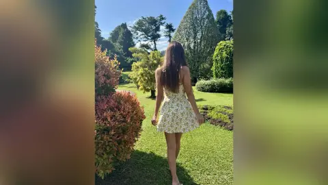 Woman in a floral summer dress walking through a lush green garden on a sunny day.