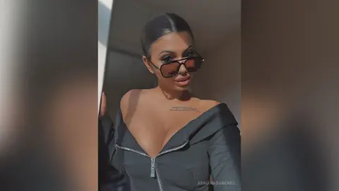 Stylish woman in a black zip-up top and sunglasses posing with a confident mood in soft natural lighting.