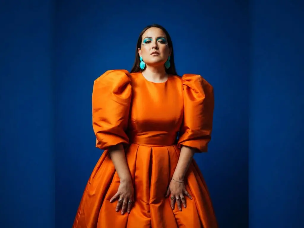 Elegant woman in a bright orange puff-sleeve satin gown posing against a deep blue studio background.