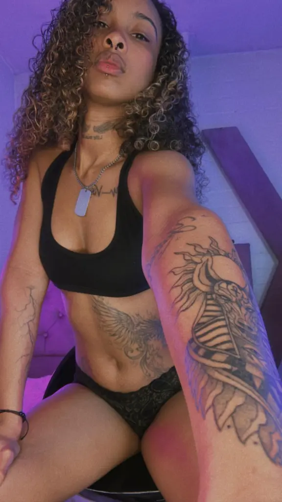 Triipsy — Tattooed woman in a black crop top and lace briefs posing under purple mood lighting.