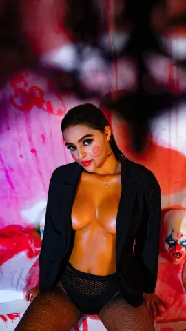 Glamorous woman in a black blazer and fishnet stockings posing against a vibrant pink abstract background.