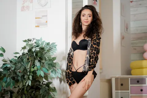 Curvy woman in black lingerie and leopard print robe posing in a bright, modern minimalist bedroom.