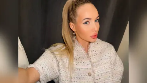 MarryDavies poses in a light-colored tweed jacket with her blonde hair pulled back in a high ponytail.