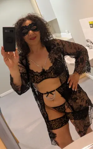 Woman in black lace lingerie and sheer robe posing in a bathroom mirror for a glamorous selfie.