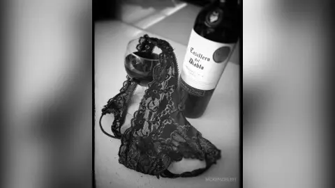 Black lace lingerie set placed next to a bottle of Casillero del Diablo wine on a table in moody black and white.